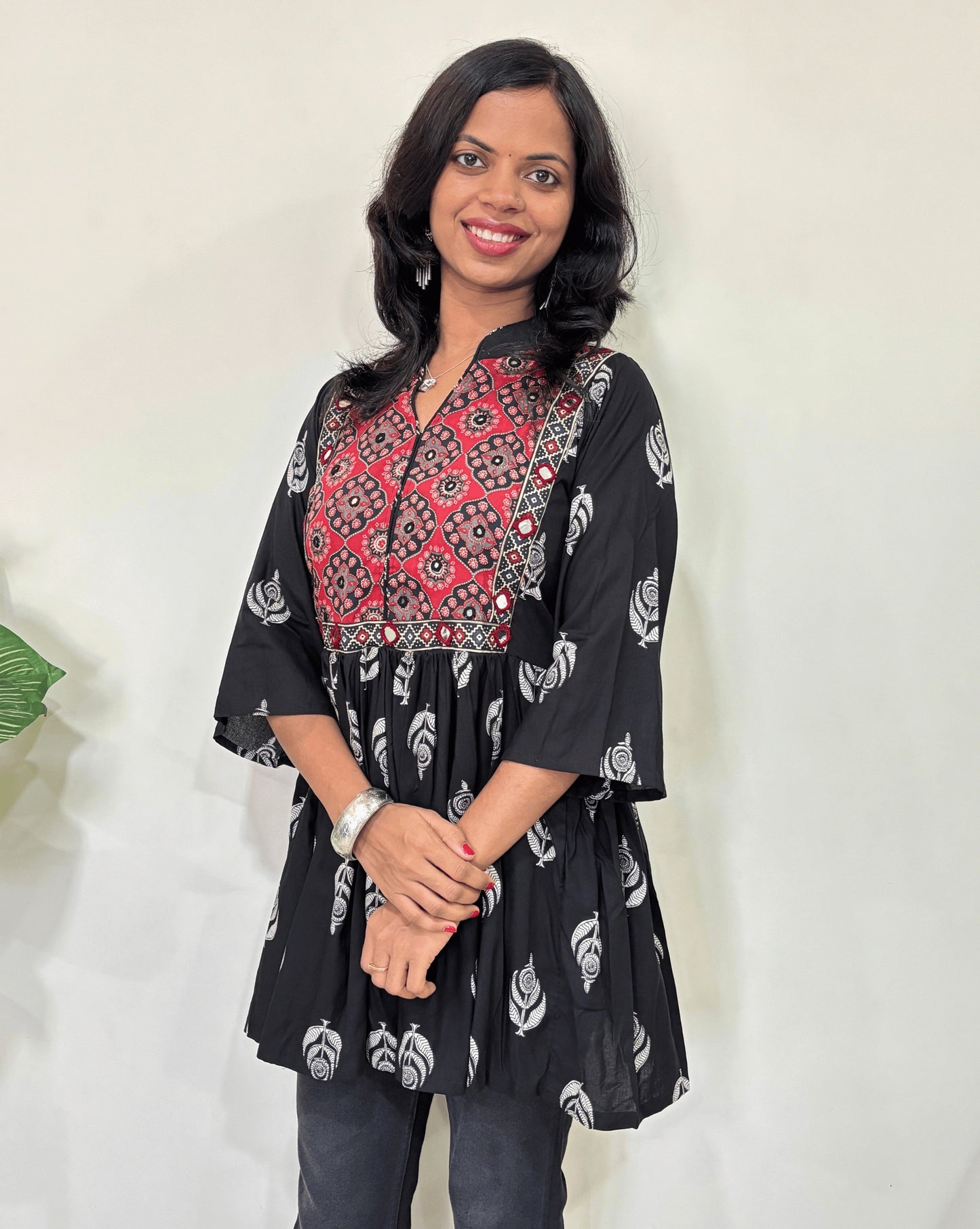 Close up of Black Ajrakh plant based Rayon cotton short kurti with Black and Red leaf patterned, V-neck with Mandarian collar, loose sleeves with hand-mirror work on chest , against a white background.
