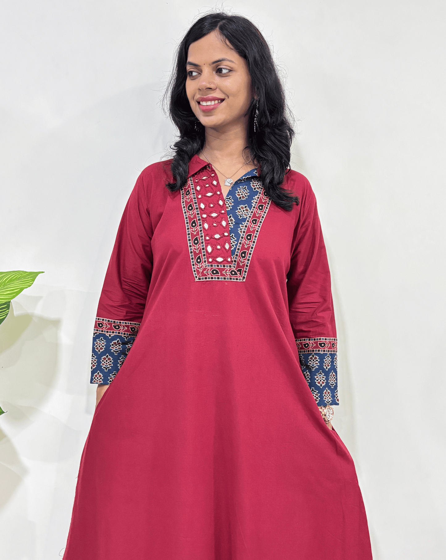 A Red women's cotton one-peice with intricate ajrakh patterns, along with 2 side pocket , Standing in front of white wall.