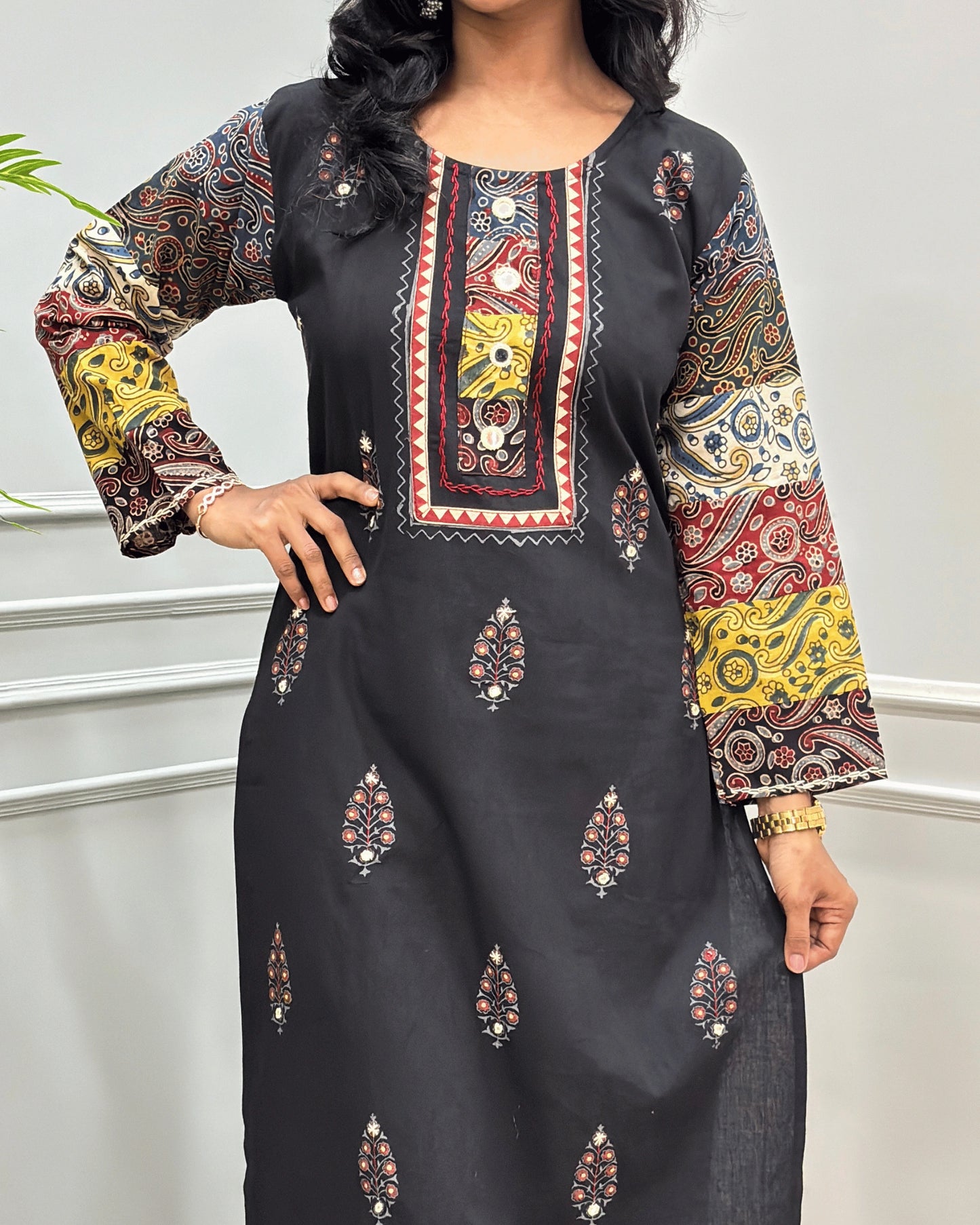 Close-up of Green Rayon Cotton Co-Ord Set with intricate multicolor printed patterns on Full-sleeves, neckline with block , and Hand-mirror motifs on the front, standing against a light gray paneled wall.