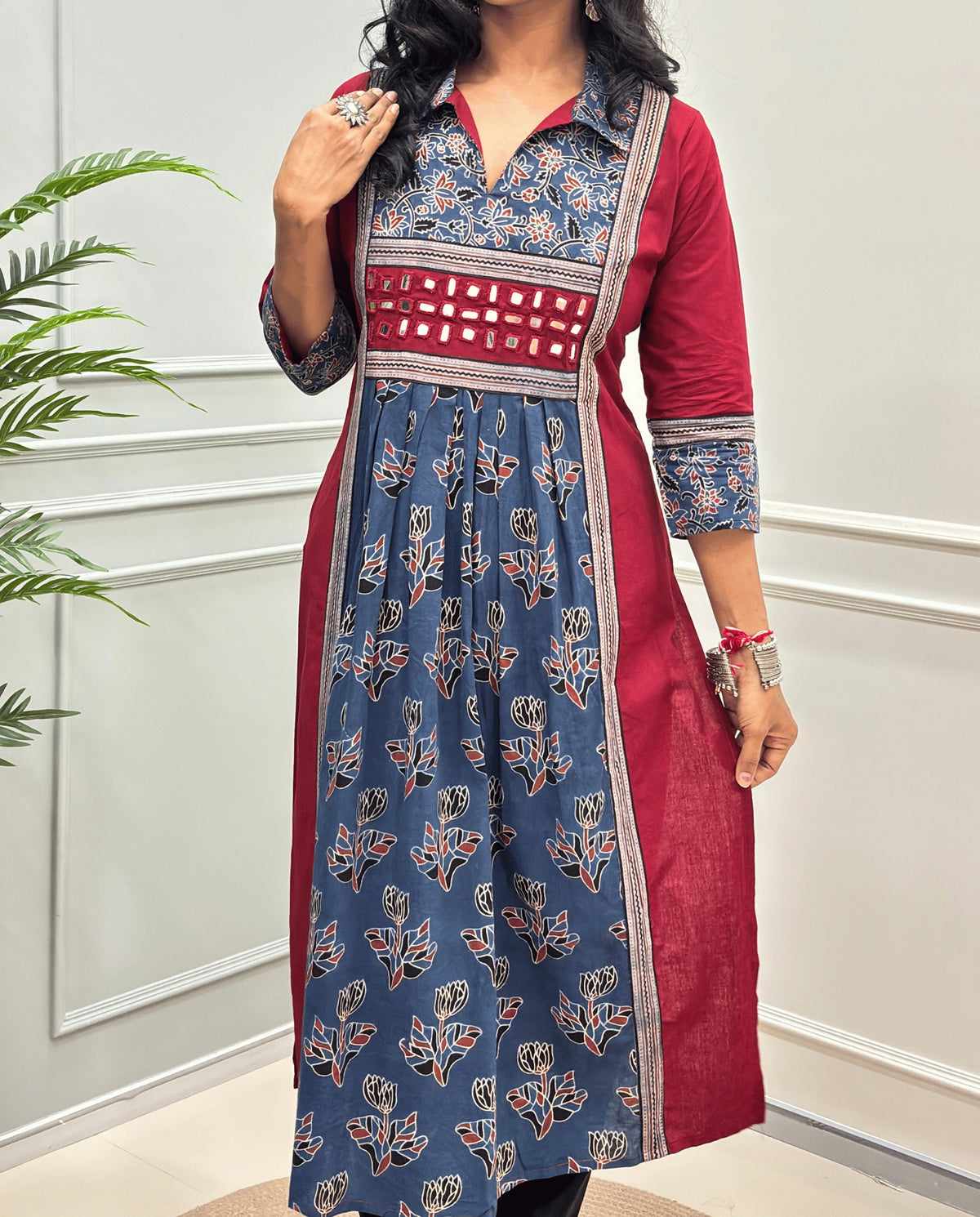 Close-up of Blue Ajrakh plant based cotton long-kurti consisting a Red colour and a matching blue floral printed frill.  blue and gold printed yoke panel, three-quarter sleeves with matching prints, and a hand-mirror work waistband, Collar V-neck .