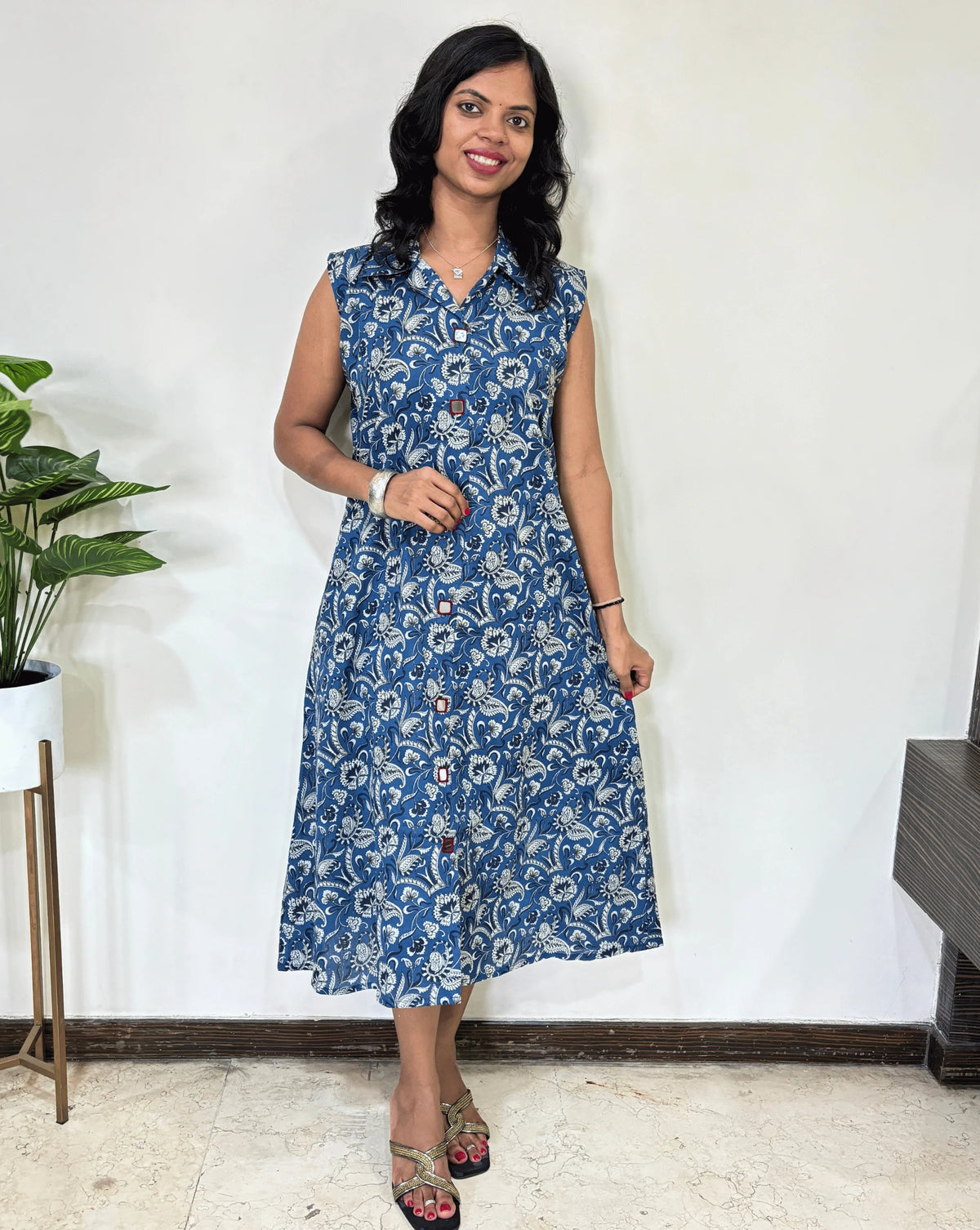 Blue Women Ajrakh Vegetable dyed plant based cotton Long Kurti with a white abstract print, Standing against a white wall with a plant to her left.