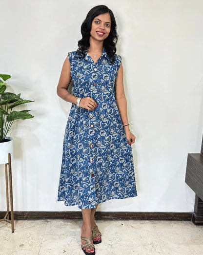 Blue Women Ajrakh Vegetable dyed plant based cotton Long Kurti with a white abstract print, Standing against a white wall with a plant to her left.