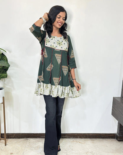Green Women's Ajrakh Vegetable Dyed Plant based Cotton Short Kurti with three quarter sleeves . White & Green base & geometric print on Sleeves & front , Standing in front of white wall. 