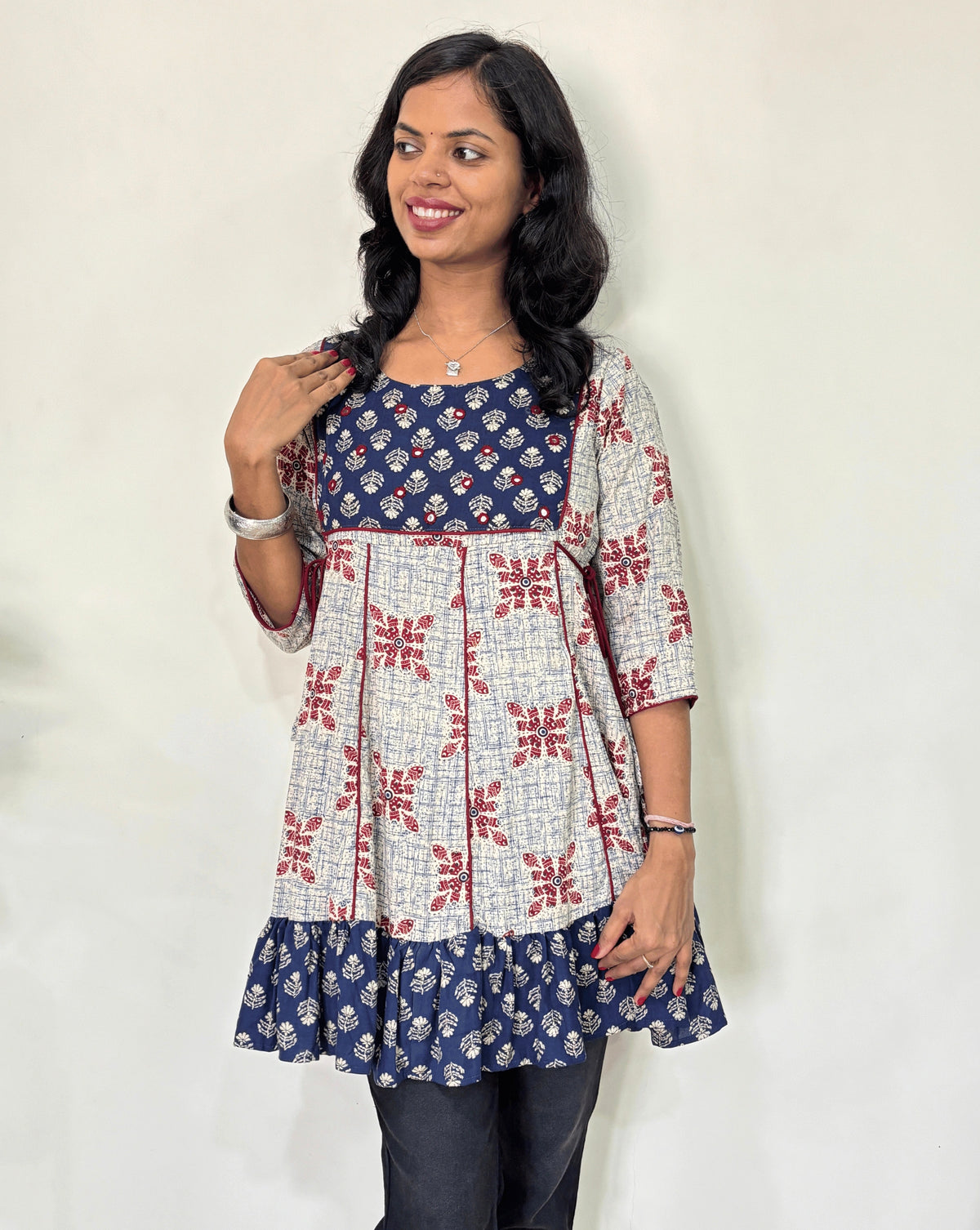 Front veiw of White Ajrakh Plant based cotton Short kurti featured with blue and white geometric print & aline frill patterned dress,  standing against a white wall.
