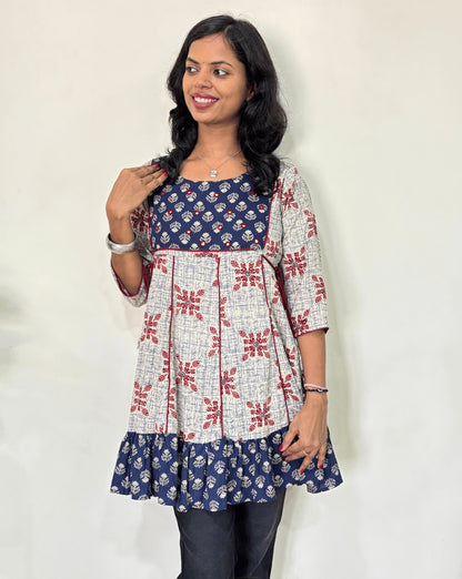 Front veiw of White Ajrakh Plant based cotton Short kurti featured with blue and white geometric print & aline frill patterned dress,  standing against a white wall.