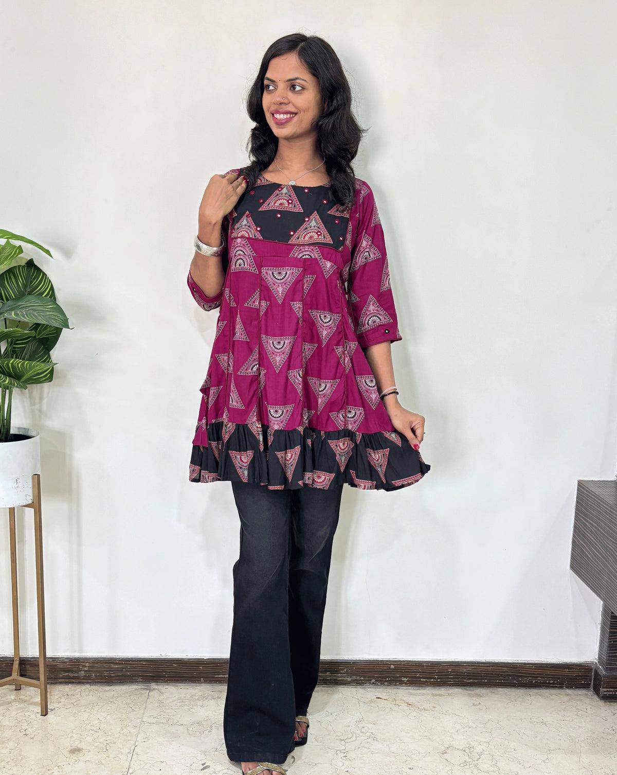 Magenta Women's Ajrakh Vegetable Dyed Plant based Cotton Short Kurti with three quarter sleeves . black & Magenta base & geometric print on Sleeves & front , Standing in front of white wall. 