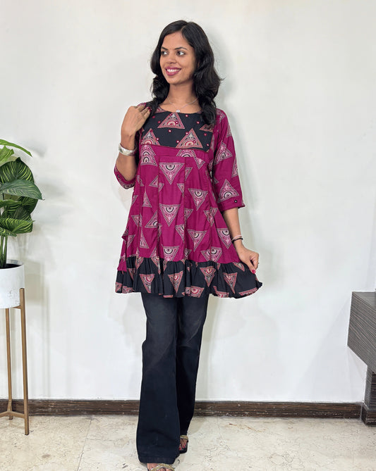 Magenta Women's Ajrakh Vegetable Dyed Plant based Cotton Short Kurti with three quarter sleeves . black & Magenta base & geometric print on Sleeves & front , Standing in front of white wall. 