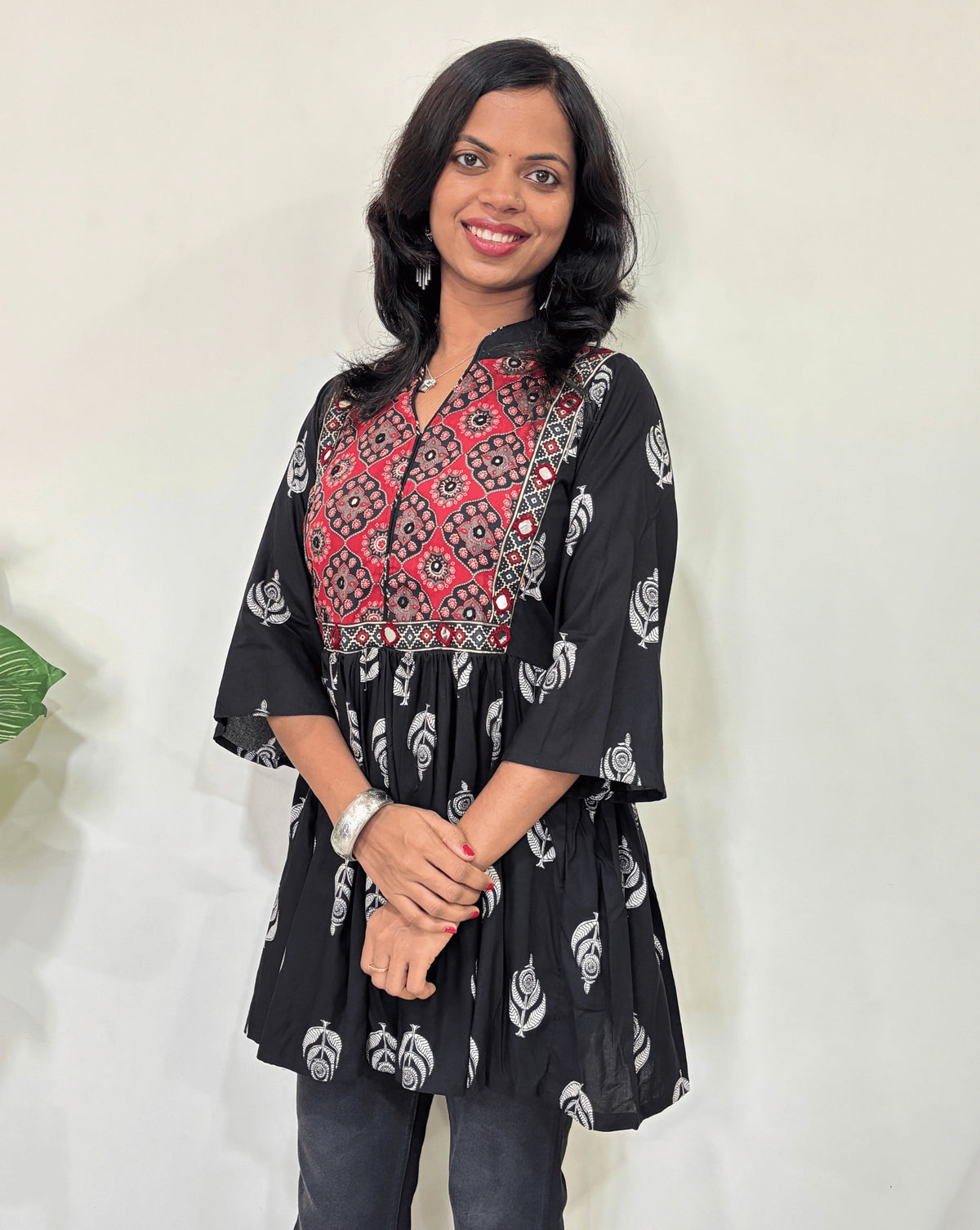 Close up of Black Ajrakh plant based Rayon cotton short kurti with Black and Red leaf patterned, V-neck with Mandarian collar, loose sleeves with hand-mirror work on chest , against a white background.