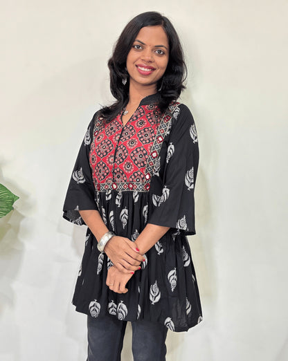 Close up of Black Ajrakh plant based Rayon cotton short kurti with Black and Red leaf patterned, V-neck with Mandarian collar, loose sleeves with hand-mirror work on chest , against a white background.