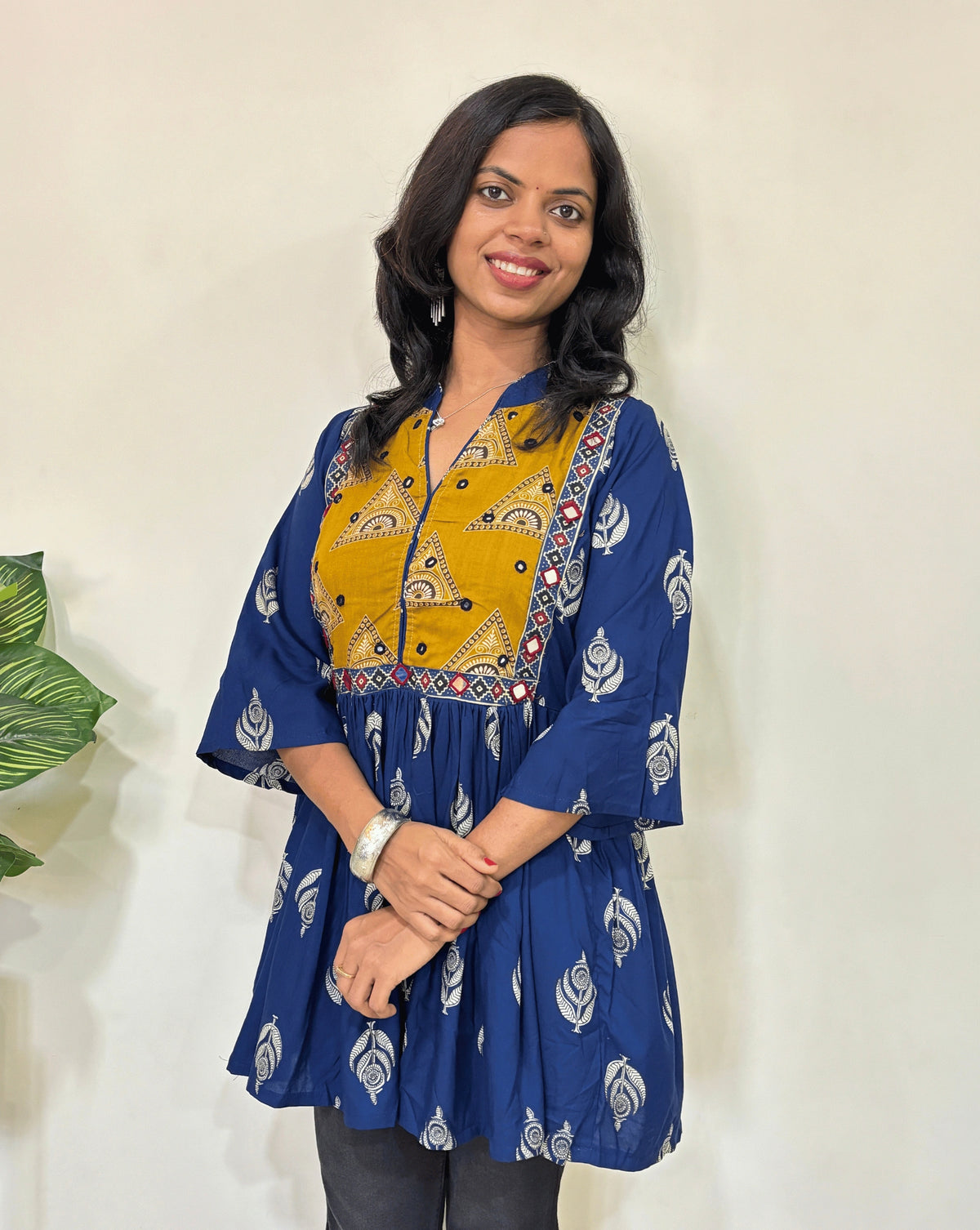 Close up of Blue Ajrakh plant based Rayon cotton short kurti with Blue and yellow leaf patterned, V-neck with Mandarian collar, loose sleeves with hand-mirror work on chest , against a white background.