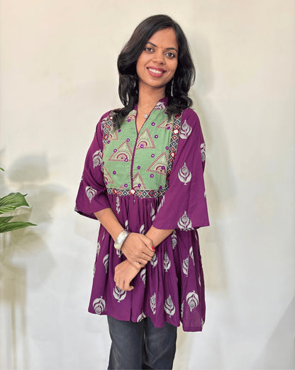 Close up of purple Ajrakh plant based Rayon cotton short kurti with purple and green leaf patterned, V-neck with Mandarian collar, loose sleeves with hand-mirror work on chest , against a white background.