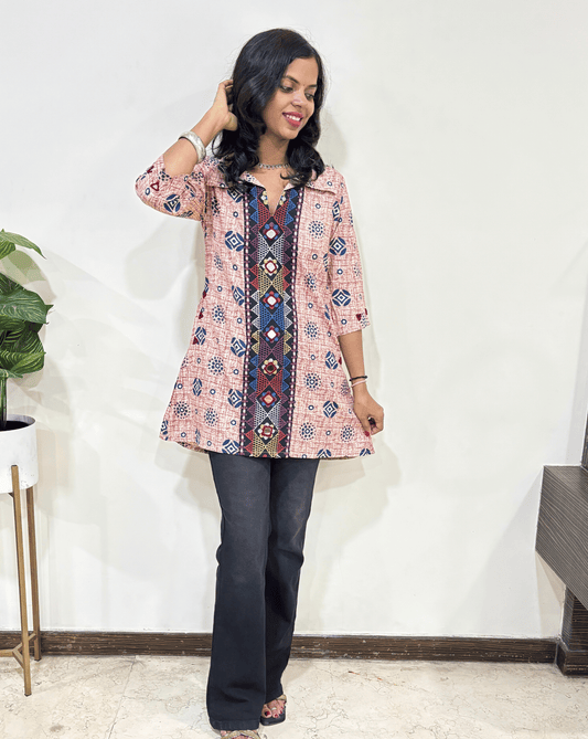 Red Women's Ajrakh Vegetable dyed plant based Cotton Short A-line kurti with multi colour embroidery panel, paired with dark pants against a white wall.