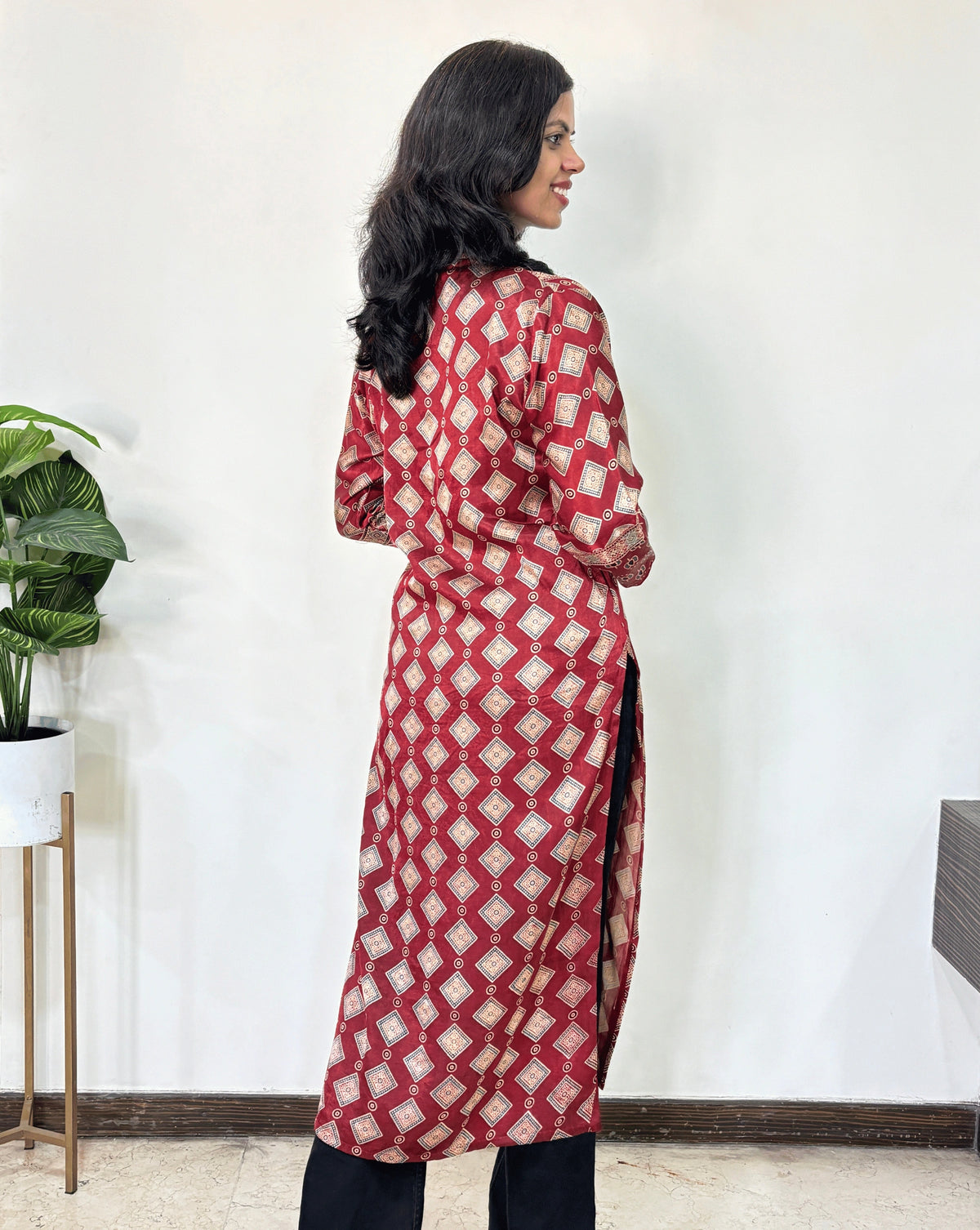 Back view of red Woman's Ajrakh Pure Mashru Silk Long-Kurti featured V-shaped neck & Three-Quarter Sleeves with Ajrakh geometric print , standing against a white wall