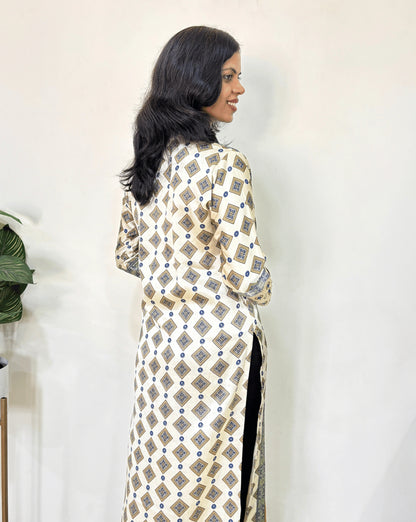 Back view of yellow- white  Woman's Ajrakh Pure Mashru Silk Long-Kurti featured V-shaped neck & Three-Quarter Sleeves with Ajrakh geometric print , standing against a white wall