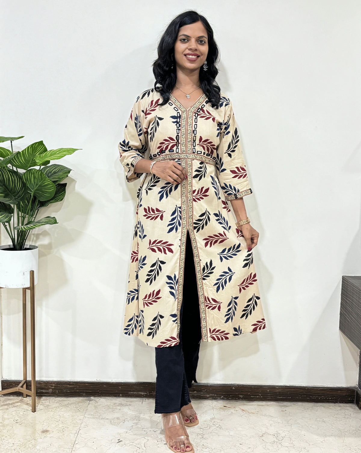 Beige Woman's Ajrakh Vegetable dyed Planet based cotton Long-kurti with a leaf print along with Ajrakh print on border from V-shaped neck on front & Sleeves cuffs, standing indoors with a plant and white wall in the background.