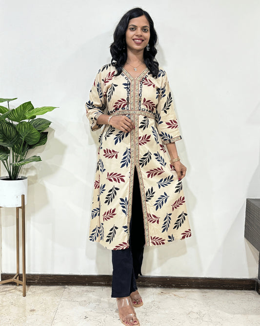 Beige Woman's Ajrakh Vegetable dyed Planet based cotton Long-kurti with a leaf print along with Ajrakh print on border from V-shaped neck on front & Sleeves cuffs, standing indoors with a plant and white wall in the background.