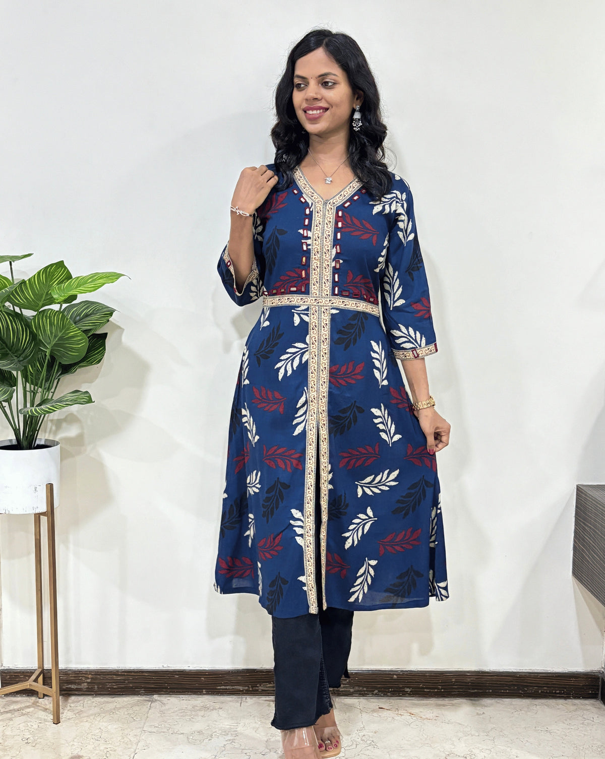 Blue Woman's Ajrakh Vegetable dyed Planet based cotton Long-kurti with a leaf print along with Ajrakh print on border from V-shaped neck on front & Sleeves cuffs, standing indoors with a plant and white wall in the background.