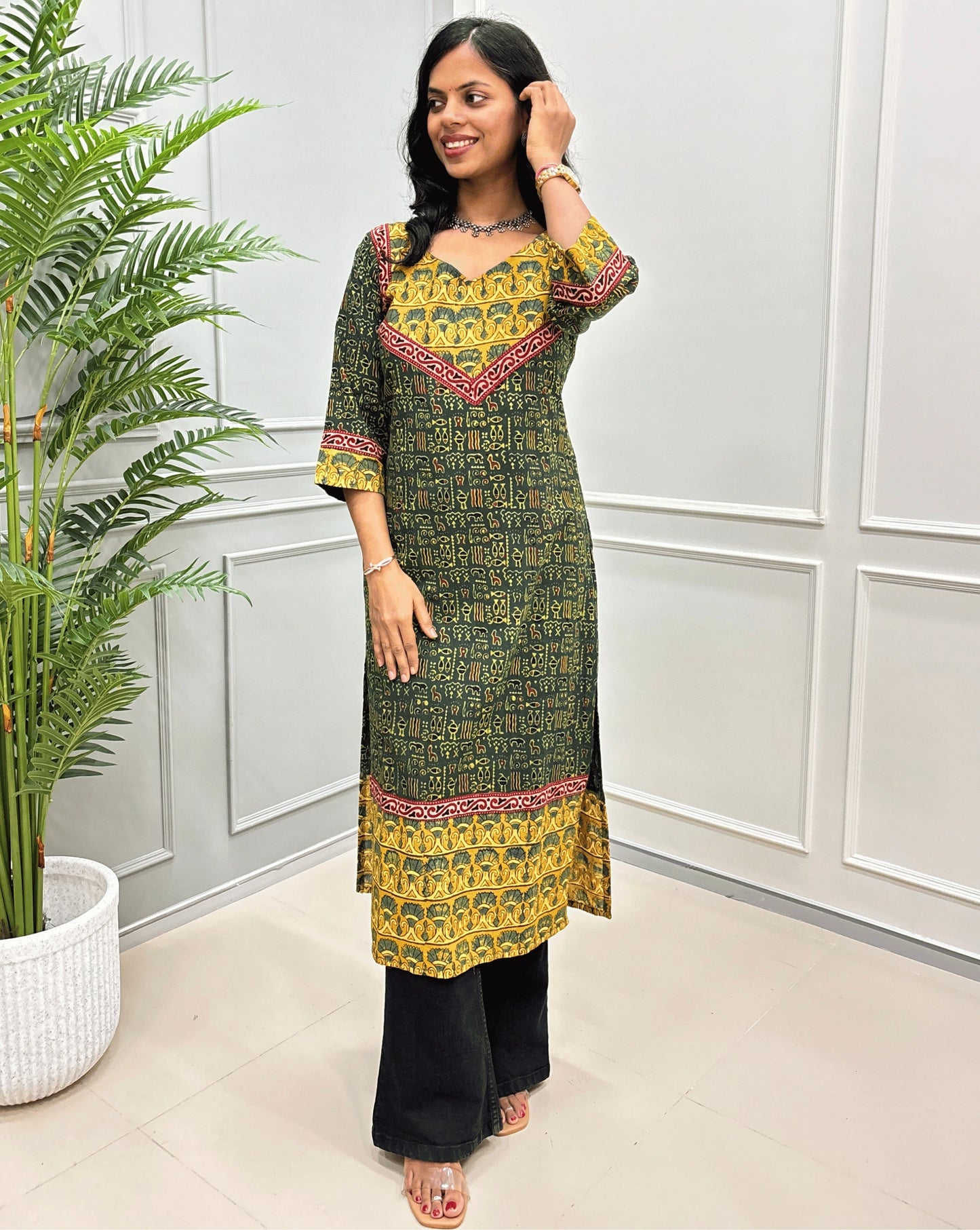 Front view of Green ajrakh handblock Cotton long-kurti with geometric print, red border-line on the front and sleeves, paired with Black flared jeans.