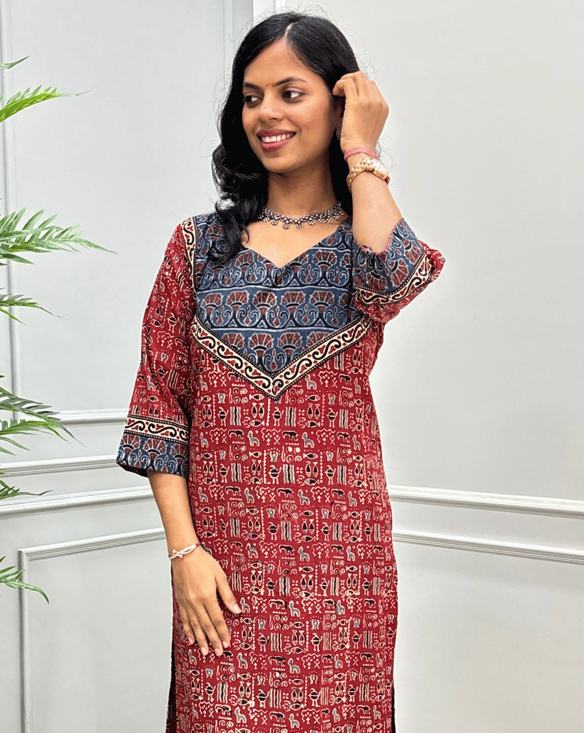 Close-up look of Red hand-block ajrakh long-kurti detail in cuved- v neck, floral ajrakh print on chest and sleeves cuffs, paired with black flared jeans. 