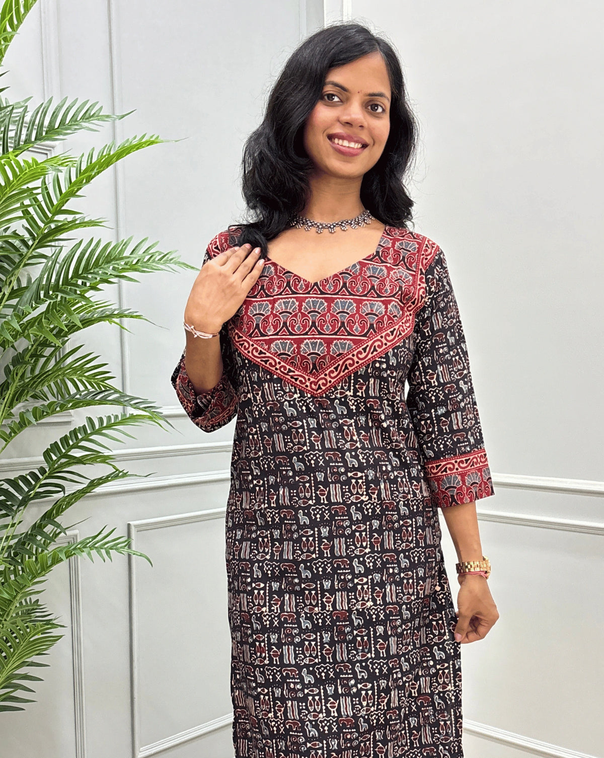 Close-up look of Black hand-block ajrakh long-kurti detail in curved- v neck, floral ajrakh print on chest and sleeves cuffs, paired with black flared jeans. 
