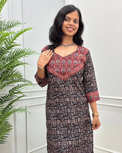Close-up look of Black hand-block ajrakh long-kurti detail in curved- v neck, floral ajrakh print on chest and sleeves cuffs, paired with black flared jeans. 