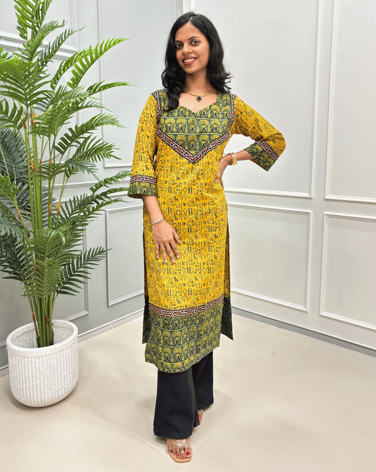 Close-up look of Yellow hand-block ajrakh long-kurti detail in cuved- v neck, floral ajrakh print on chest and sleeves cuffs, paired with black flared jeans. 