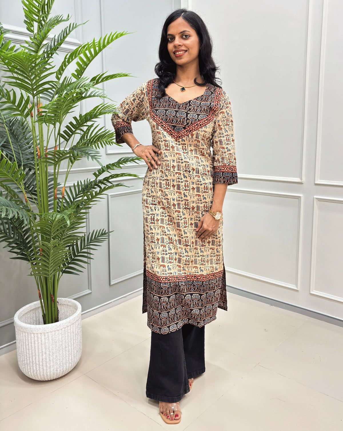 Close-up look of Beige hand-block ajrakh long-kurti detail in curved- v neck, floral ajrakh print on chest and sleeves cuffs, paired with black flared jeans. 
