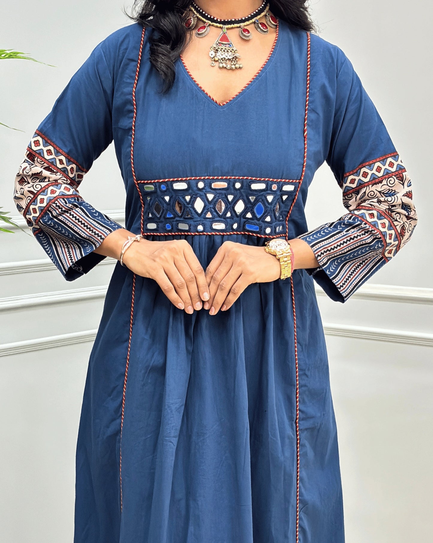 Close-up of hand-block  mirror work on blue Ajrakh cotton kurti with intricate multicolor geometric embroidery on the sleeves and a matching embroidered band at the waist, styled with jewelry.