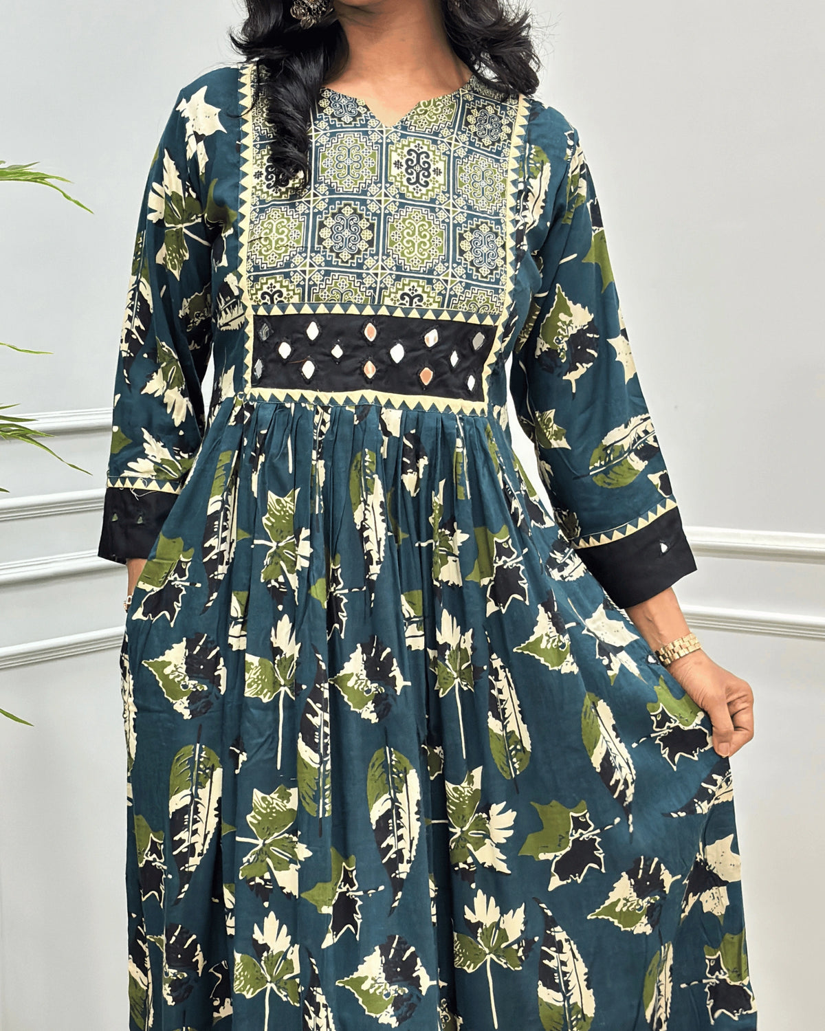 Close-up of Green Ajrakh Plant based cotton Long-kurti featured with three-quarter sleeves , Ajrakh print on curved V-neck-line , hand-mirror work on front chest & sleeves cuffs, Beautiful leaf print on dress along with pocket.