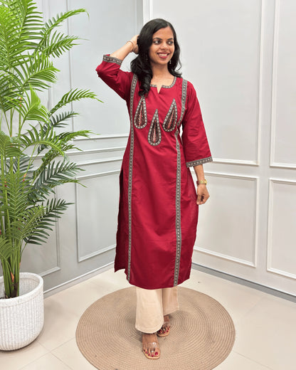 Red Women's Ajrakh Pure Cootn Long-kurti with Beige and Black Ajrakh print with Palm-leaf detailing , paired with beige pants, standing in a room with a potted plant and paneled wall