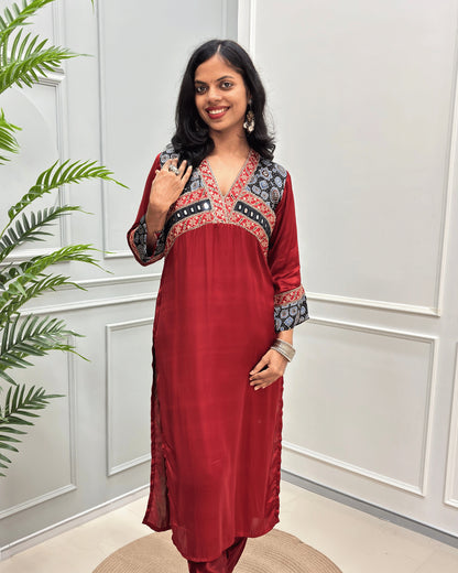 Front view of Deep-Red women's Ajrakh Modal Silk Long kurti featured with Black base & ajrakh print on neck & cuffs , hand-mirror work on chest standing in a white paneled room.