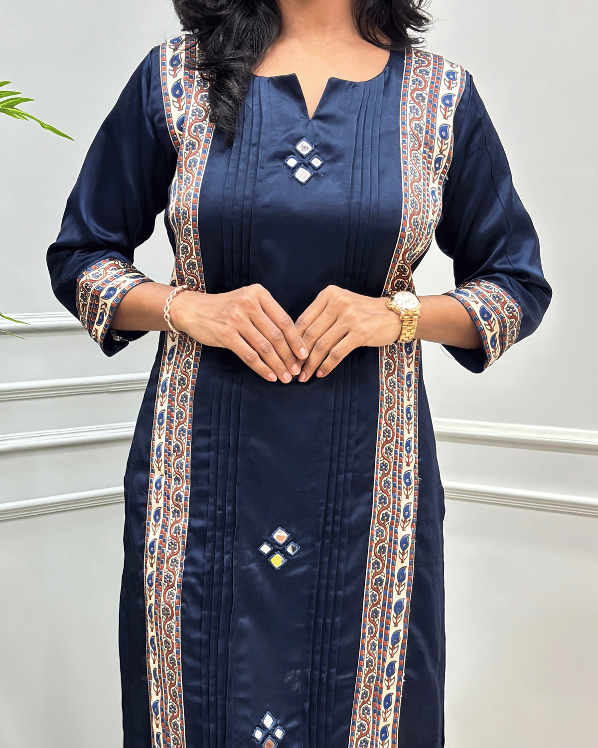 Close-up of Navy-Blue women's Ajrakh Mashru Silk Long-kurti with intricate gold, beige, and blue patterned borders down the front and on the sleeves, Hand-mirror work on front , Round-V- neck paired with gold jewelry.