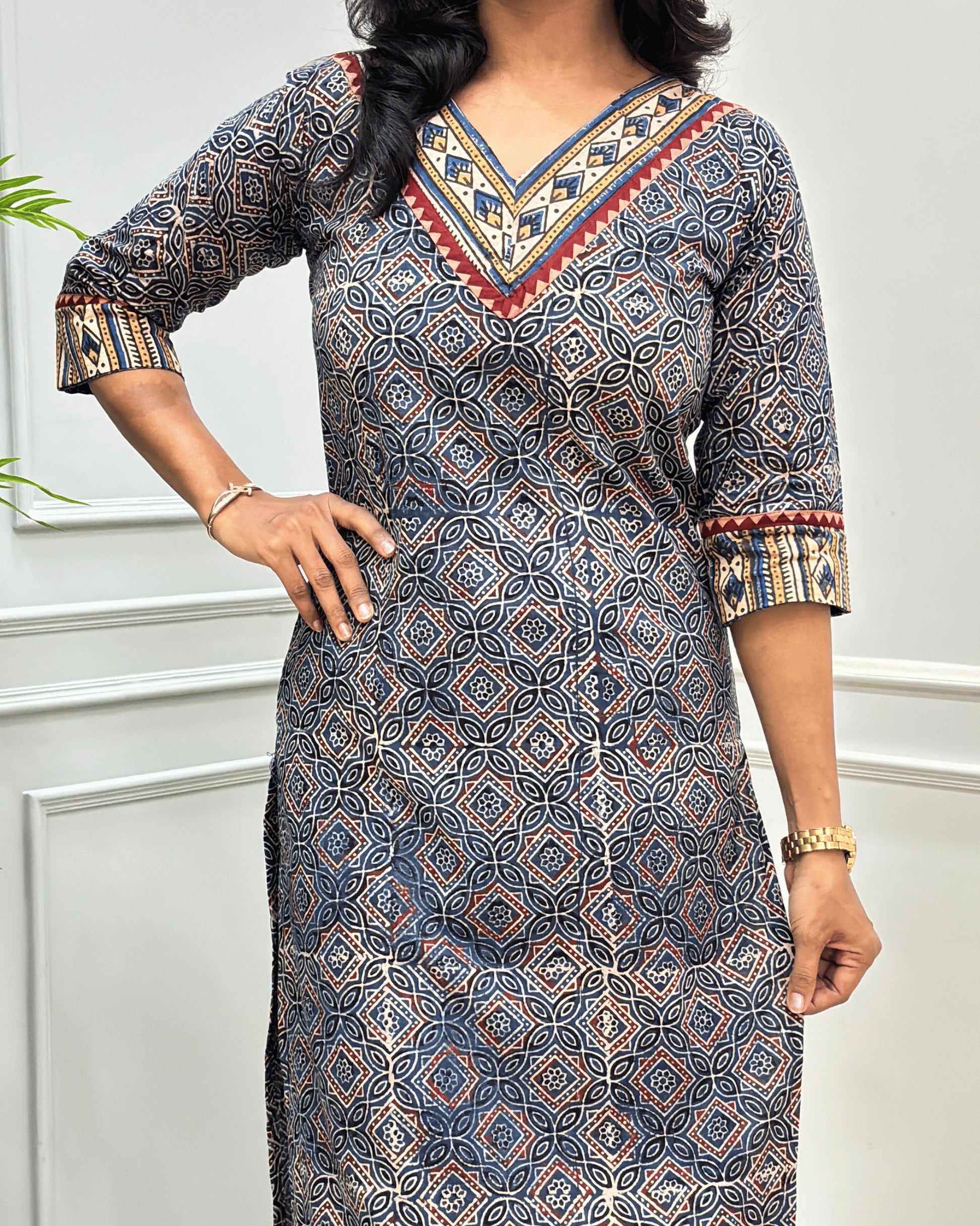 Close-up of Blue and Beige Hand-block Ajrakh pure cotton Long-kurta with a Ajrakh geometric pattern, featuring a V-neckline and patterned sleeve cuffs, standing against a white paneled wall