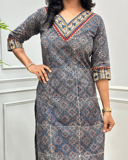 Close-up of Blue and Beige Hand-block Ajrakh pure cotton Long-kurta with a Ajrakh geometric pattern, featuring a V-neckline and patterned sleeve cuffs, standing against a white paneled wall