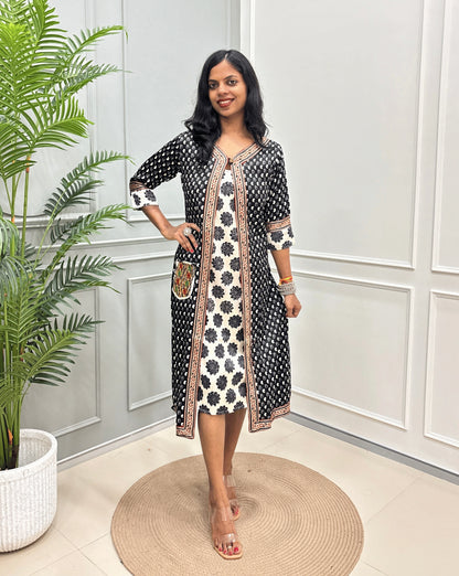 Black women's Ajrakh pure Mashru silk Long one-peice with Black Shrug attach with White inner consist floral print wiith black colour , standing in a decorated room with a potted plant and paneled wall