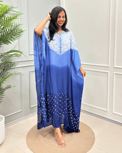 Blue Women's Ajrakh Pure Modal Silk Kaftan with a 3 shades of Blue with ajrakh print on chest & Bandhani Small dots with white on Bottom, standing on a round woven rug in front of a white paneled wall.
