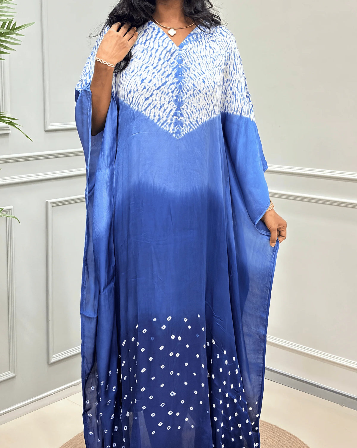 Closed-up View of Blue Women's Ajrakh Pure Modal Silk Shibori Kaftan Featured with Long-length, with a 3 shades of Blue with ajrakh print on chest & Bandhani Small dots with white on Bottom Along with Full Sleeves & Free Size,  standing on a round woven rug in front of a white paneled wall.
