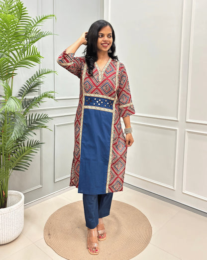 Blue Women's Ajrakh pure cotton 2 peice Co-Ord set with a Red base & an abstract of blue & Beige Bandhani print on Front Chest to Side & Sleeves , standing on a round woven mat in front of a white paneled wall with a potted plant.