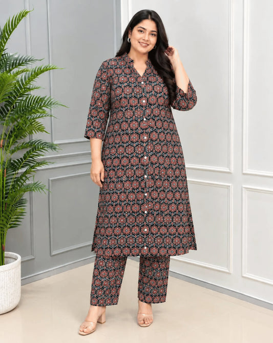 Black Women's Ajrakh Aline Cotton Long 2 peice Cord set Featured with Collar neck with an all-over geometric Ajrakh print in dark brown, rust red and teal, along with same printed bottom, standing in a studio with paneled gray walls and a potted plant.