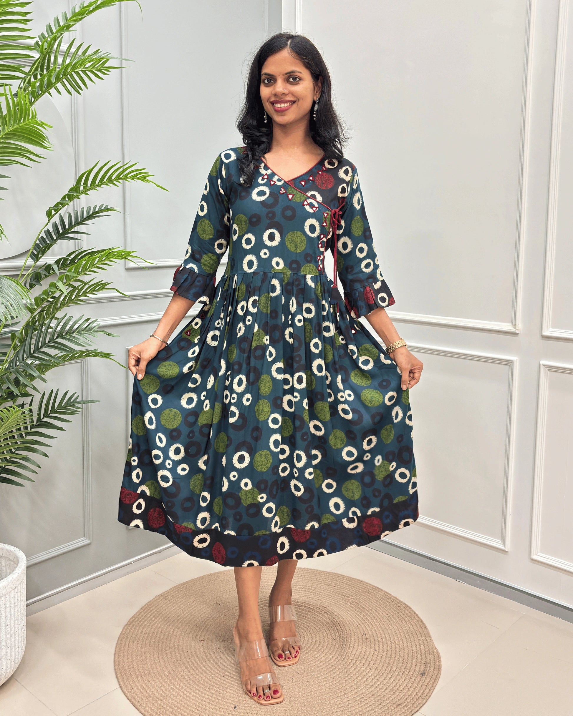 Green Women's Vegetable dyed plant based Cotton fabric with a colorful abstract print of white, green, and blue circles, standing on a round woven rug in front of a white paneled wall.