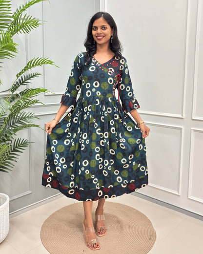 Green Women's Vegetable dyed plant based Cotton fabric with a colorful abstract print of white, green, and blue circles, standing on a round woven rug in front of a white paneled wall.