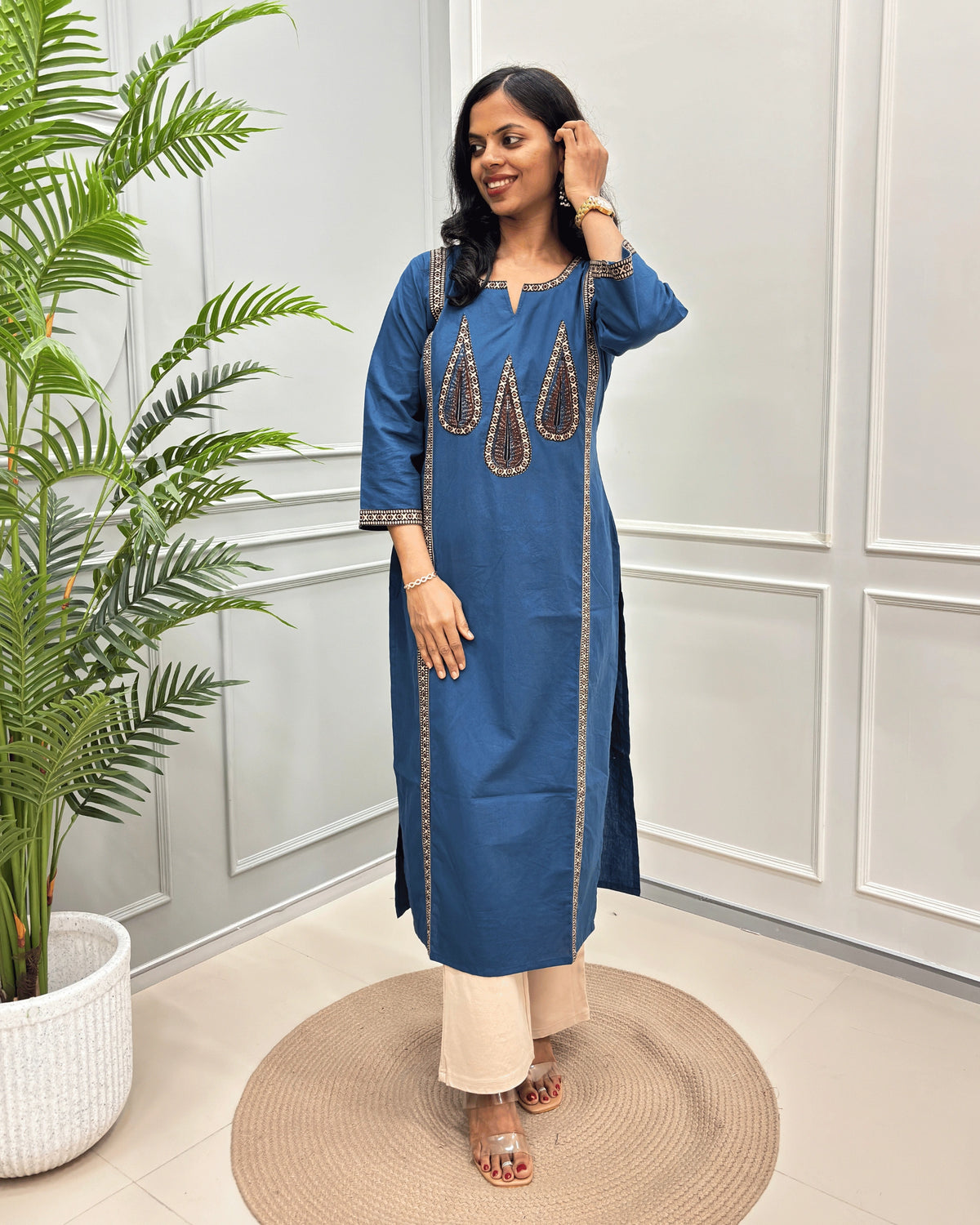 Blue Women's Ajrakh Pure Cootn Long-kurti with Beige and Black Ajrakh print with Palm-leaf detailing , paired with beige pants, standing in a room with a potted plant and paneled wall