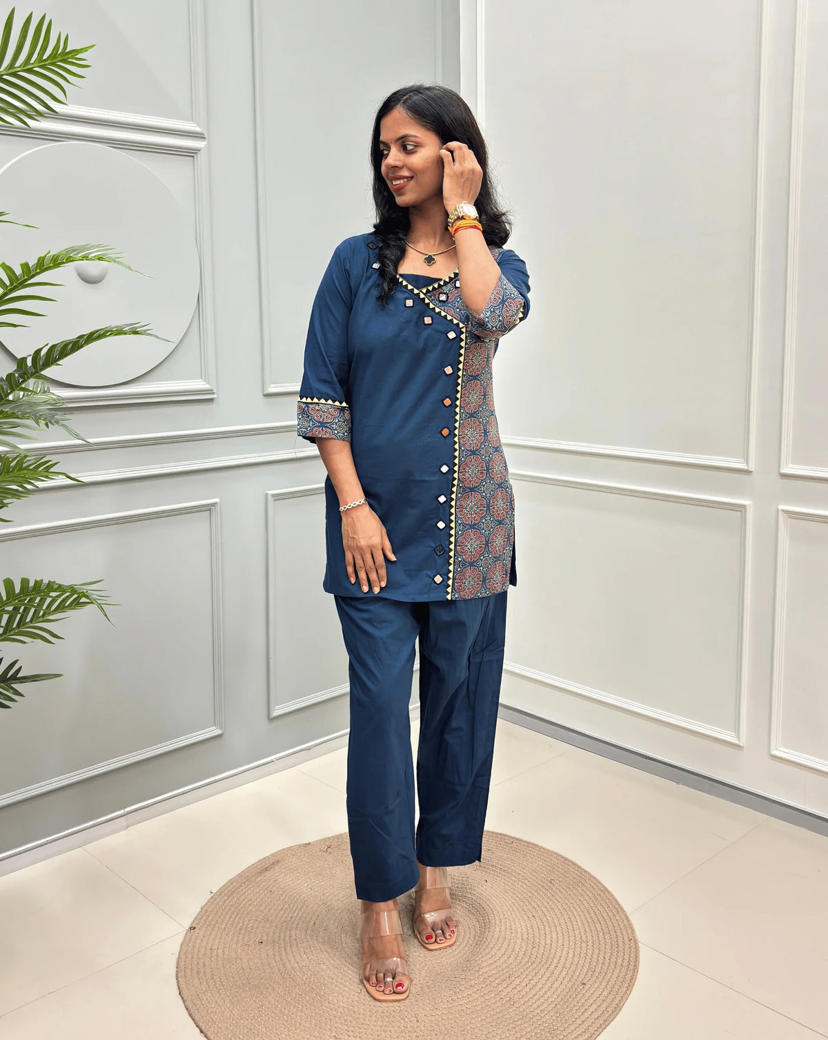 Blue Women's Ajrakh Pure Cotton 2-peice Co-Ord set with a Ajrakh printed panel on the front & Sleeves, Angrakha Patterned on front, standing on a round woven rug in a modern room with white paneled walls.