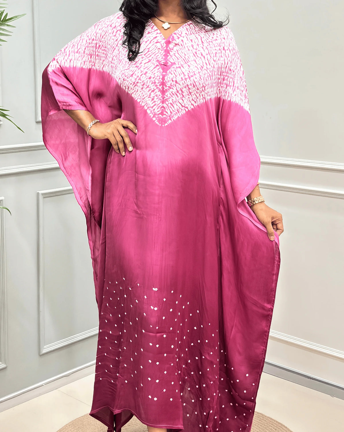 Closed-up View of Pink Women's Ajrakh Pure Modal Silk Shibori Kaftan Featured with Long-length, with a 3 shades of Pink with ajrakh print on chest & Bandhani Small dots with white on Bottom Along with Full Sleeves & Free Size,  standing on a round woven rug in front of a white paneled wall.