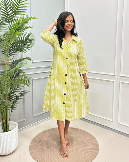 Green Women's Ajrakh A-line Pure Cotton Long Kurti with an Ajrakh Strip Print on abstract of Green, White standing on a round woven rug in front of a light gray paneled wall with a potted plant.