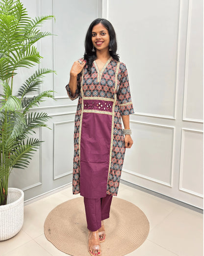 Purple Women's Ajrakh pure cotton 2 peice Co-Ord set with a black base & an abstract of blue & Red Geometric print on Front Chest to Side & Sleeves , standing on a round woven mat in front of a white paneled wall with a potted plant.
