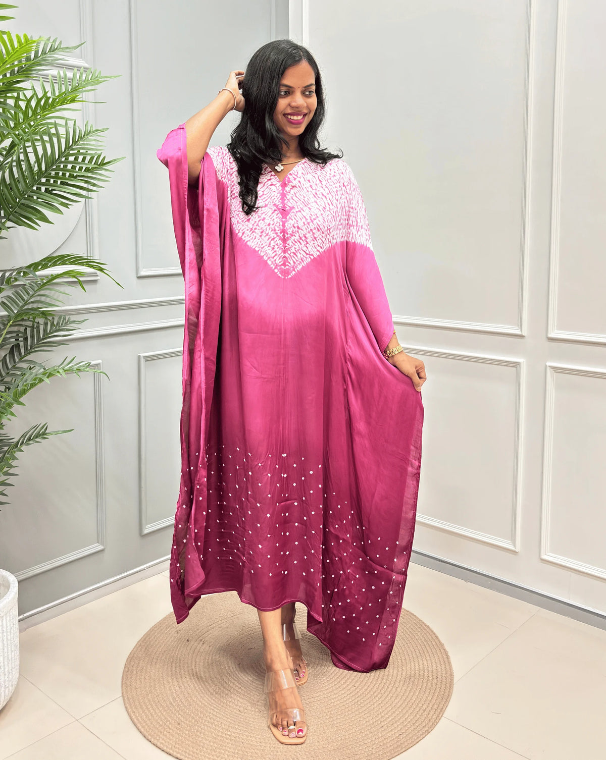 Pink Women's Ajrakh Pure Modal Silk Kaftan with a 3 shades of Pink with ajrakh print on chest & Bandhani Small dots with white on Bottom, standing on a round woven rug in front of a white paneled wall.
