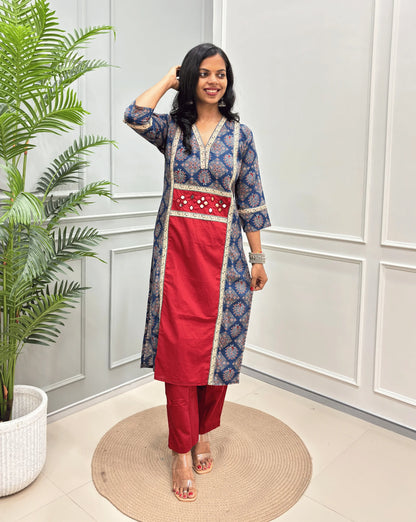 Red Women's Ajrakh pure cotton 2 peice Co-Ord set with a Blue base & an Peacock print on Front Chest to Side & Sleeves , standing on a round woven mat in front of a white paneled wall with a potted plant.