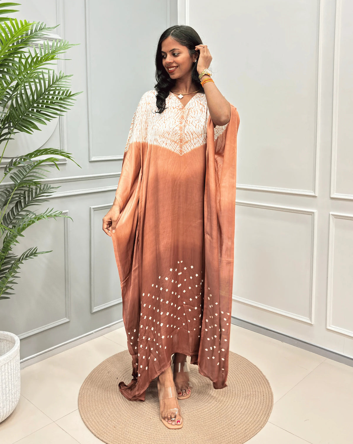 Brown Women's Ajrakh Pure Modal Silk Kaftan with a 3 shades of brown with ajrakh print on chest & Bandhani Small dots with white on Bottom, standing on a round woven rug in front of a white paneled wall.