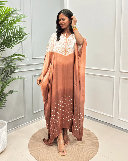 Brown Women's Ajrakh Pure Modal Silk Kaftan with a 3 shades of brown with ajrakh print on chest & Bandhani Small dots with white on Bottom, standing on a round woven rug in front of a white paneled wall.